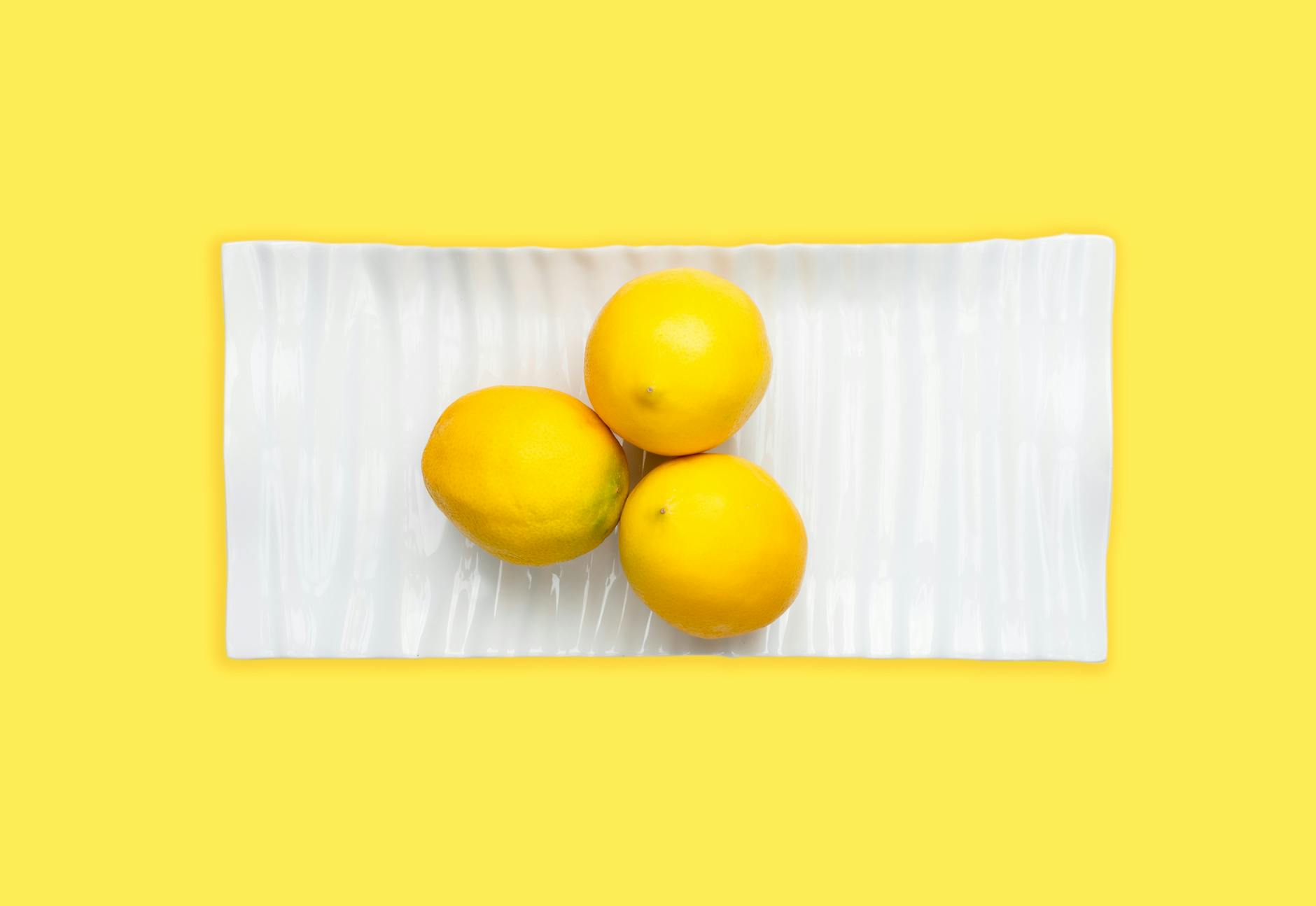 Fresh lemons arranged on white plate against vibrant yellow background, symbolizing renewed vitality and sensuality.
